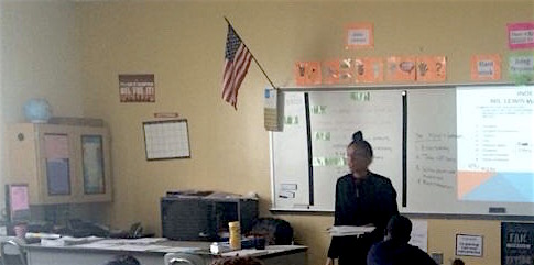 Alieyyah as a teacher standing in front of a white board at the head of a classroom