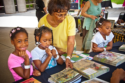 three young black girls and one black adult looking at a table of books, Knight Arts Challenge Detroit: Charles H. Wright Museum of African American History The Charles H. Wright will use the arts to foster an interest in reading by weaving interactive cultural experiences throughout the museum’s Children’s Book Fair.
