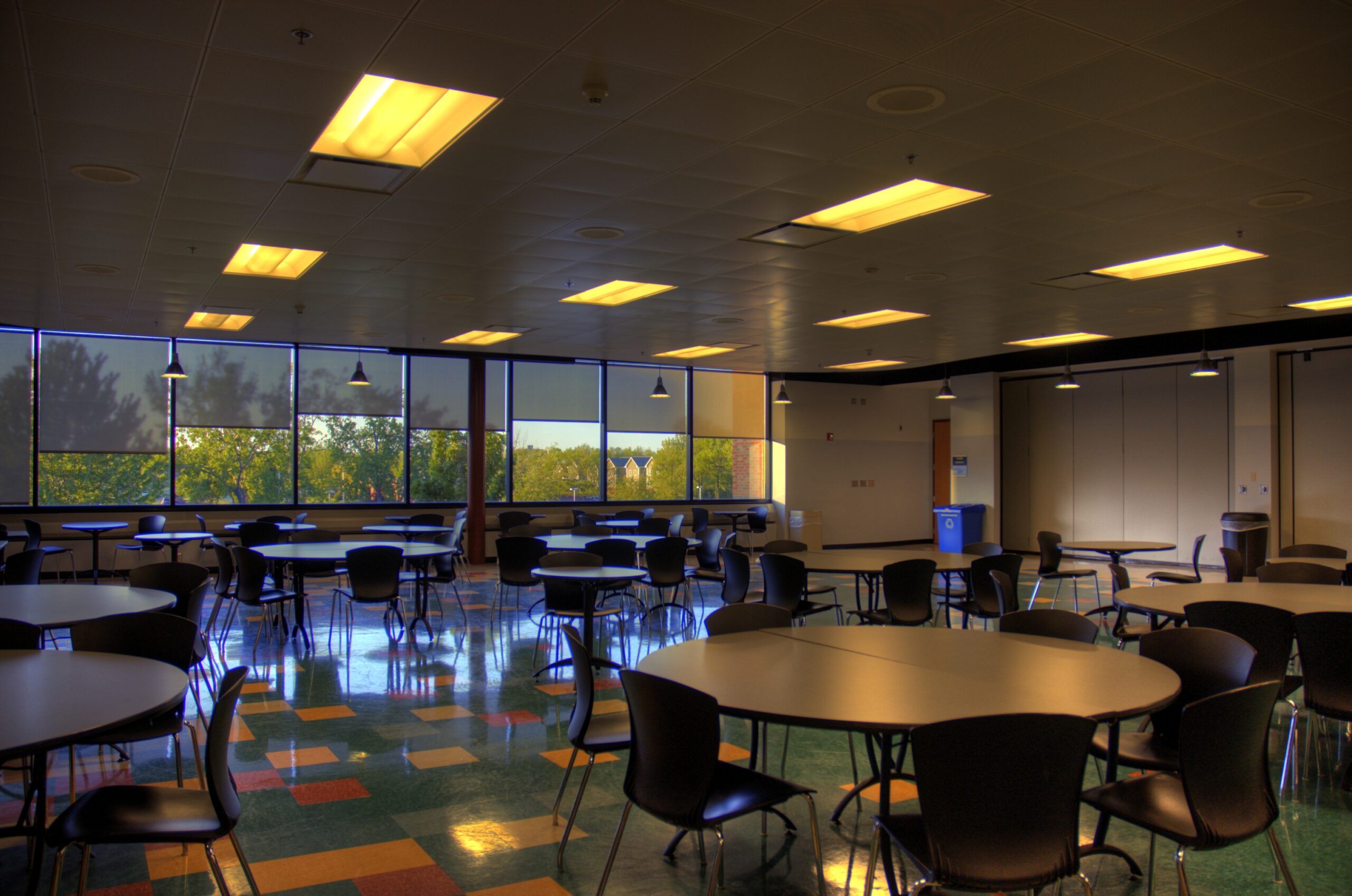Monroe Community College Cafeteria, all seats at round tables empty, yellow overhead lighting