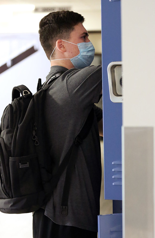 boy in a face mask wearing black backpack at a school locker