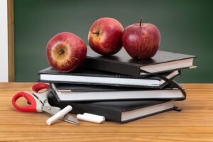 messy stack of teacher supplies, including books, chalk, and apples